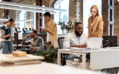 Group of employees in the office, they sit at desks, use laptops and talk